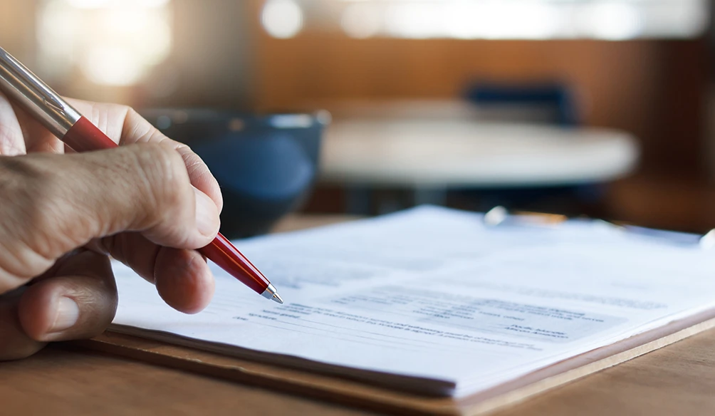 Hand holding a pen poised to sign a contract