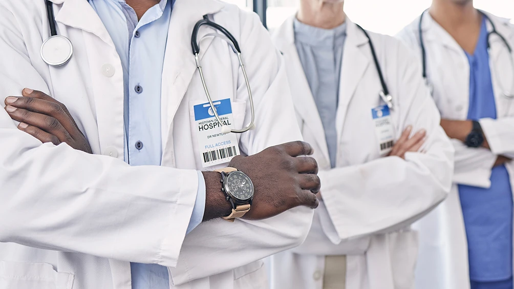 Physicians in white lap coats with stethescopes, arms crossed confidently standing together