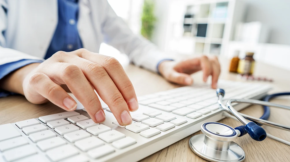 physician in background typing on keyboard with stethescope on desk